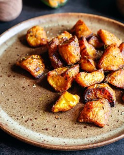 Golden brown roasted potatoes, seasoned with a blend of herbs, arranged on a rustic ceramic plate.