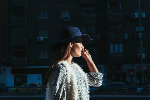 A woman in a chic hat and stylish attire enjoys a sunny morning in the city. The urban landscape