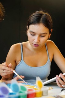 A teenage girl is intently engaged in a painting activity in an art class, using a brush, with a