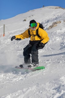 A snowboarder wearing a vibrant yellow jacket expertly glides down a snowy mountain slope. The