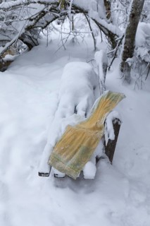 Frozen yellow towel lying on a snow covered bench in a forest near a creek