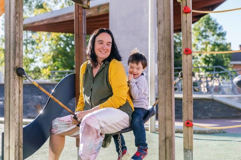 A mother and her child with Down syndrome share a joyful moment on a swing at the playground. The