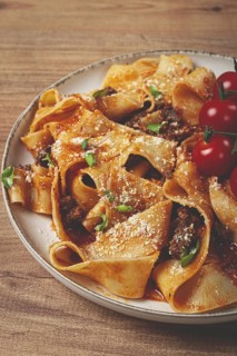Pappardelle pasta with bolognese sauce, topped with parmesan cheese and cherry branch, homemade, no