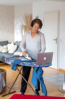 Woman, mid-50s, works from home, with laptop and communicates with colleagues via headset, home