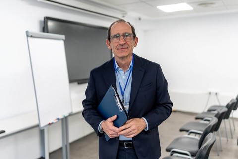Experienced businessman and professor in a suit stands confidently with clipboard, gazing at camera