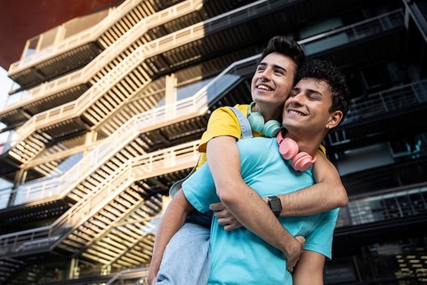 A happy gay couple shares a joyful piggyback ride against a modern urban backdrop. Their genuine