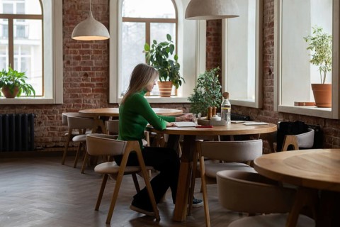 A woman in a cozy cafe with warm lighting, surrounded by rustic brick walls and lush green plants,