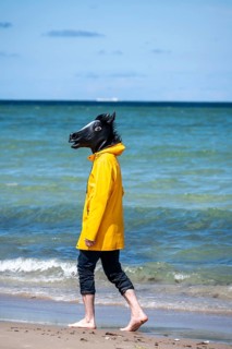 Person with horse mask on the beach, bizarre scene, Denmark