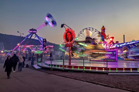 Colourful rides and lights illuminate the fair at dusk and full of movement, carousel and hustle