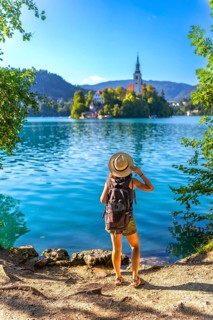 Female tourist with backpack and hat admiring the assumption of mary pilgrimage church on lake bled