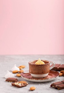 Cup of hot chocolate and pieces of milk chocolate with almonds on a gray and pink background. side