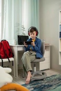 A young boy, wearing headphones, deeply focused on playing a game on his smartphone while sitting