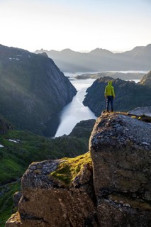 Mountaineer, young man standing on rocks and looking into the distance, at sunrise, fjord