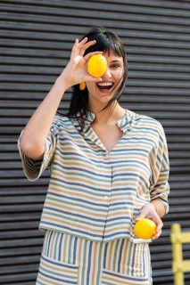 Joyful woman in striped outfit holding lemons, symbolizing freshness and happiness. Her smile