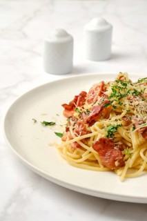 Close-up view of freshly prepared spaghetti carbonara topped with crispy bacon pieces, grated