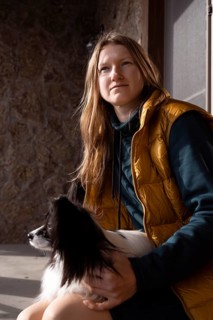 A person in a yellow vest sits with their purebred papillon dog on their lap, capturing a serene