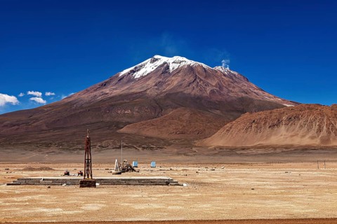 Isolated landscape with a large, snow-covered volcano and a small tower-like structure, the town of