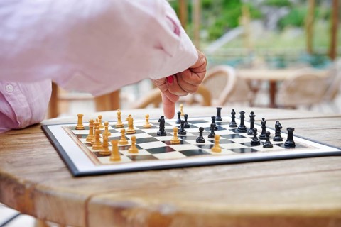 A person engaged in an outdoor chess game, showcasing strategic hand movement over a wooden table