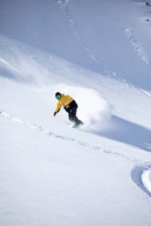 A snowboarder in a yellow jacket expertly navigates a snowy mountain slope, kicking up fresh powder