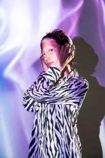 A young, trendy woman poses confidently in a zebra print shirt, illuminated by soft purple and blue