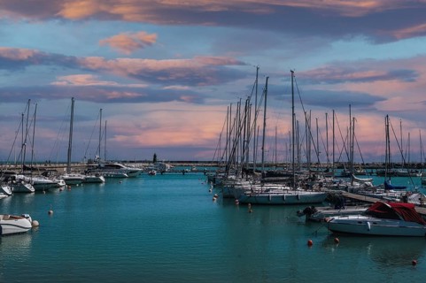 Sailboats gently bob in a serene harbor near Civitanova Marche, Italy. The sky is painted with warm