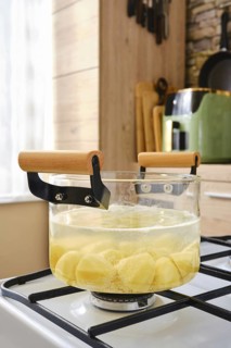 A glass pot filled with chopped potatoes simmers on a stove in a warm kitchen. The bright light