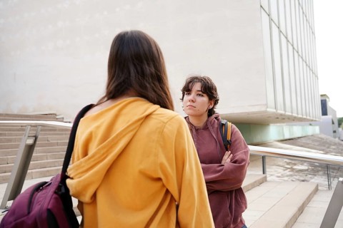 Two teenagers, a non-binary individual and a female, engage in conversation after returning to