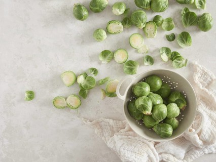 A bunch of fresh green raw brussels sprouts on the countertop, others in a colander. Top view