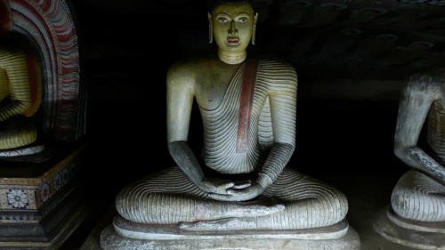 Seated Buddha statue in deep meditation surrounded by darkness, Dambulla cave temple, Sri Lanka