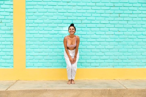 A joyful young Latin woman poses against a colorful turquoise and yellow brick wall in the vibrant