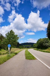 Cycle path, country road and blue sky with cumulus clouds in a landscape near Biederbach, Black