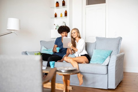 A couple sits comfortably on a stylish gray sofa, enjoying each other's company while browsing a