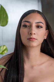 Portrait of a woman with long dark hair and subtle makeup, gazing off camera. Soft natural light