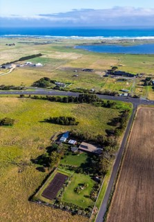 Aerial image showcases vast coastal farmland with a winding road, distant ocean, and cloudy sky in