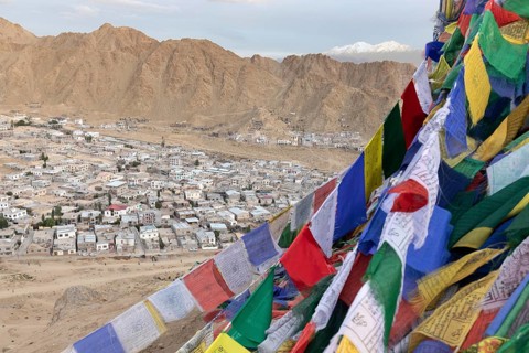 A stunning panorama of Leh, Ladakh, India, features vibrant Tibetan prayer flags fluttering in the