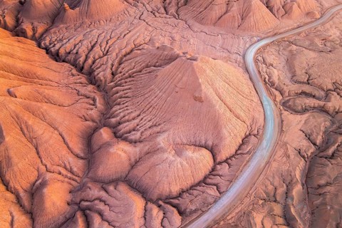 A stunning aerial view of a red desert landscape features undulating hills and a winding road in