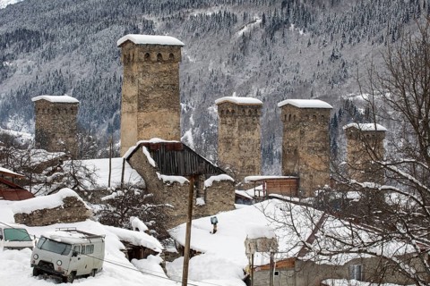 Stone watchtowers stand tall in a snow-covered village, nestled amidst mountainous terrain in