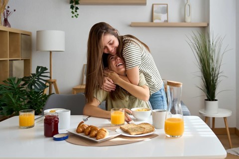 A happy lesbian couple shares a warm embrace during breakfast in a bright, cozy kitchen The scene