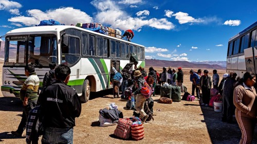 Travelers load luggage on a bus in a dry desert landscape in bright sunshine, bus station in the