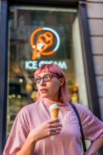 Modern female millennial with pink colored hair and modern hair cut eating ice cream in the city