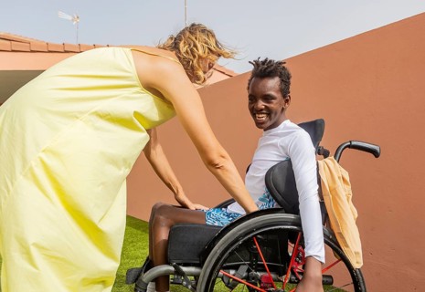 A person helps a boy in a wheelchair with cerebral palsy in pool. The scene depicts camaraderie and
