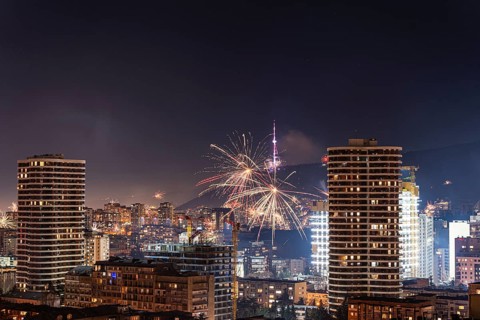 A vibrant display of fireworks illuminates the night sky over Tbilisi's downtown. Skyscrapers and