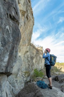Brave female hiker standing on cliff edge, adjusting safety helmet with determination. Majestic