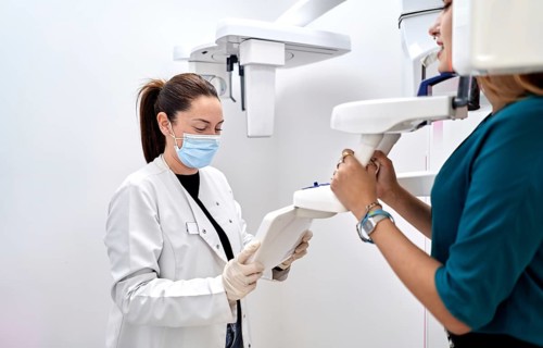 Dentist in a white coat and face mask assists a patient with modern dental equipment in a bright