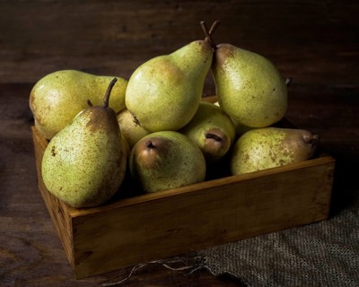 A collection of ripe pears arranged in a rustic wooden box, set on a dark wooden table. The scene