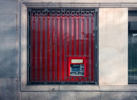 A striking image capturing a red ATM machine securely located behind ornate, patterned iron bars on