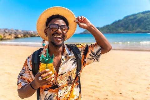 Young black man wearing a straw hat and sunglasses, savoring a refreshing pineapple cocktail while