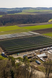 Large solar system in a field surrounded by green countryside and forests, Agri PV Bau für