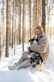 A woman lovingly hugs her black and white Border Collie in a wintery forest setting. They enjoy a