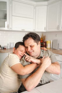 A touching moment as a father and son embrace in a well lit kitchen. The scene exudes warmth, love,